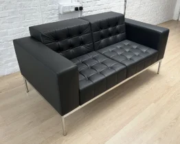 black leather two seat sofa with buttons and a chrome frame